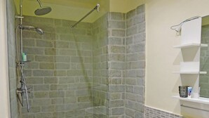 Un baño con zona de ducha, pared de piedra, un lavabo blanco y un espejo sobre el lavabo.