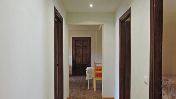 Un estrecho pasillo con puertas de madera a ambos lados, que conduce a un cuarto con una puerta de madera oscura al final.