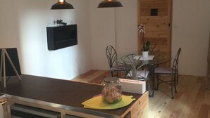 Cocina compacta con una isla de madera, dos refrigeradores, luces colgantes, una mesa de comedor con sillas y una puerta de madera.