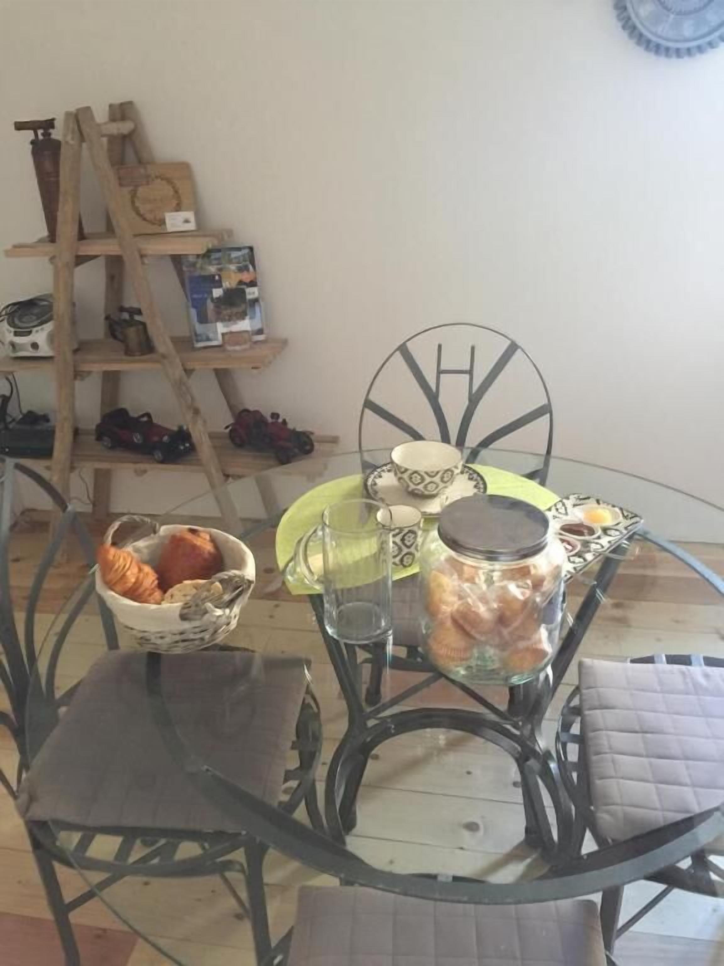 Un área de comedor con una mesa de vidrio, sillas de metal, un estante de madera con juguetes y un reloj colgado en la pared.
