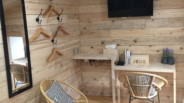 Una habitación con paredes de madera, un televisor de pantalla plana sobre un escritorio, dos sillones de mimbre y un espejo en la pared izquierda.