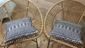Una habitación con dos sillones de mimbre con cojines estampados, una cama con cubrecama azul y un espejo en la pared.