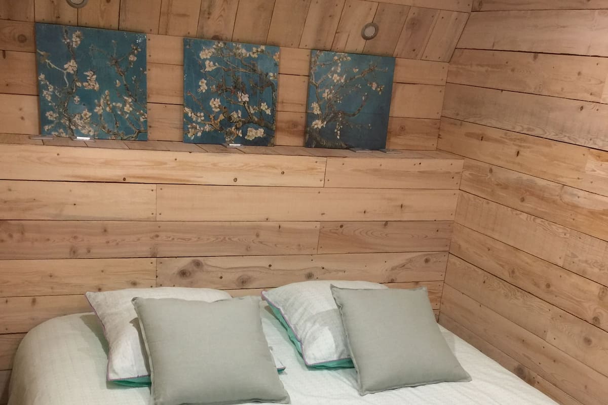 Quarto com painéis de madeira, uma cama, almofadas e obras de arte na parede.
