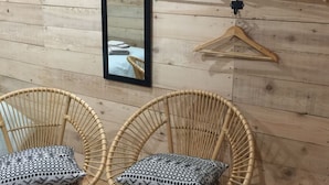 Una habitación con paredes de paneles de madera, un espejo grande y tres perchas de madera. Hay dos sillas de mimbre con cojines estampados.
