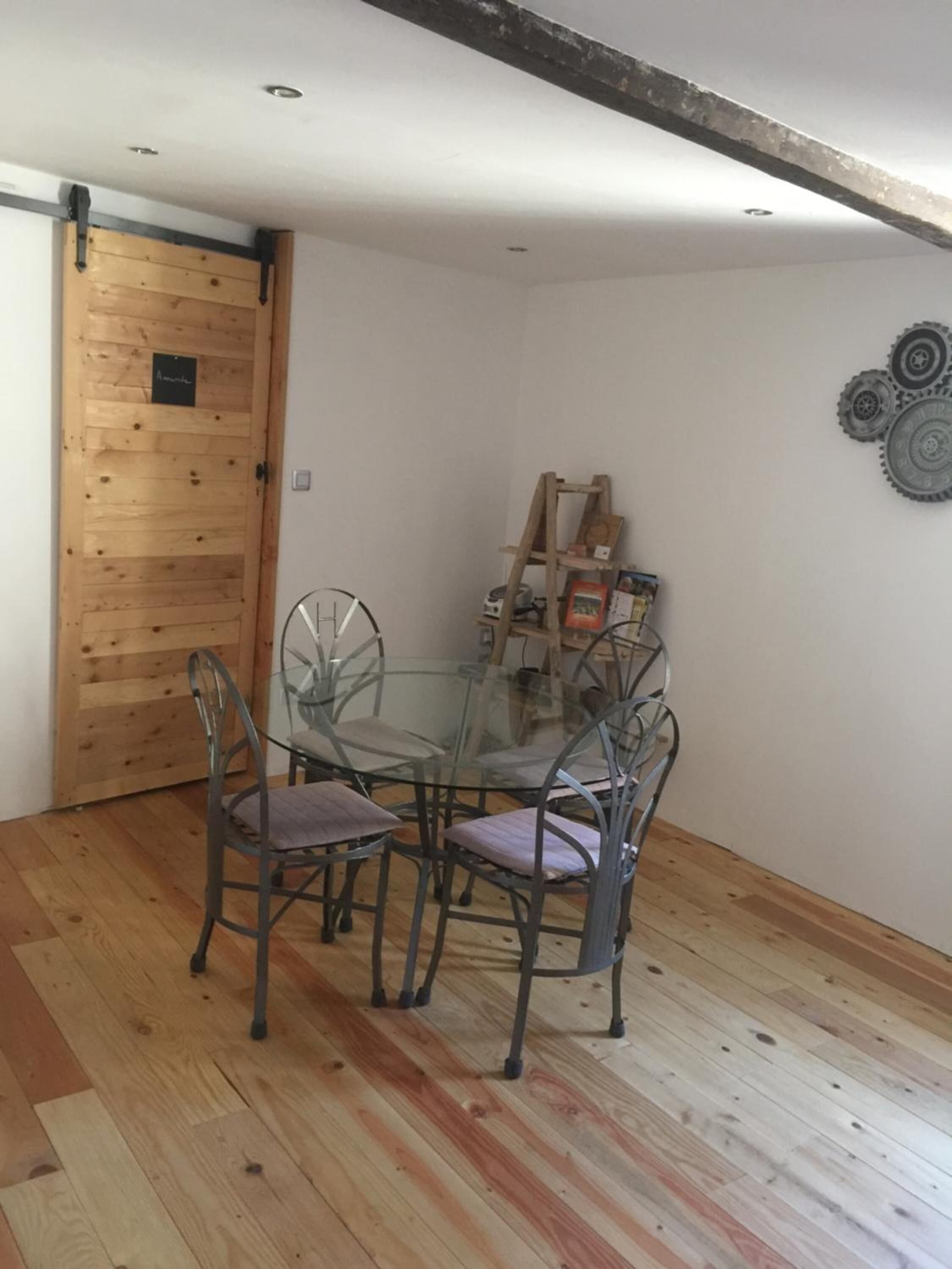 Un comedor con mesa de vidrio y sillas de metal, una puerta de madera y un adorno con forma de rueda fijado a la pared.
