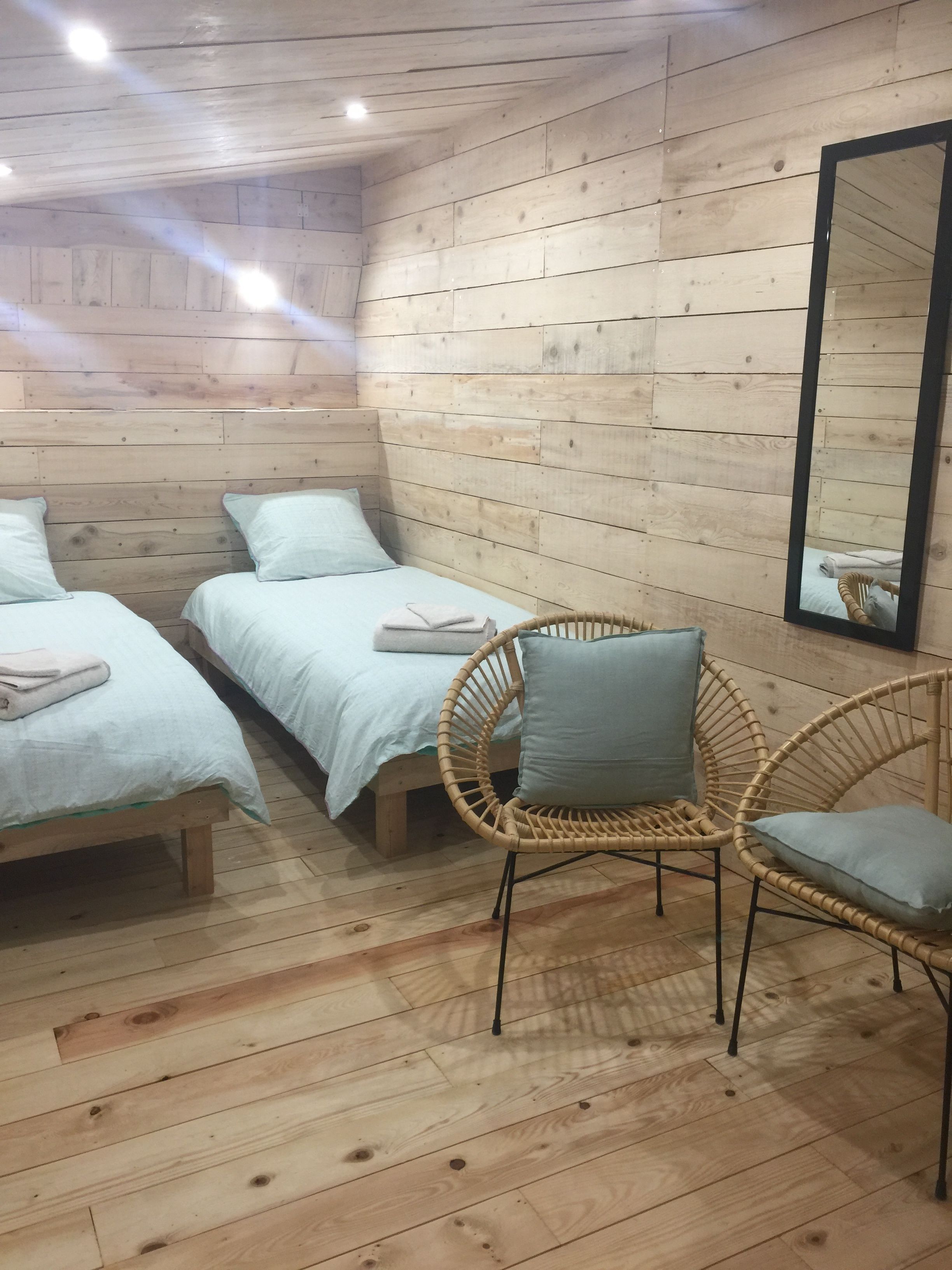 Ein Zimmer mit zwei Holzbetten, einem Korbsessel und einem Spiegel an der Wand.