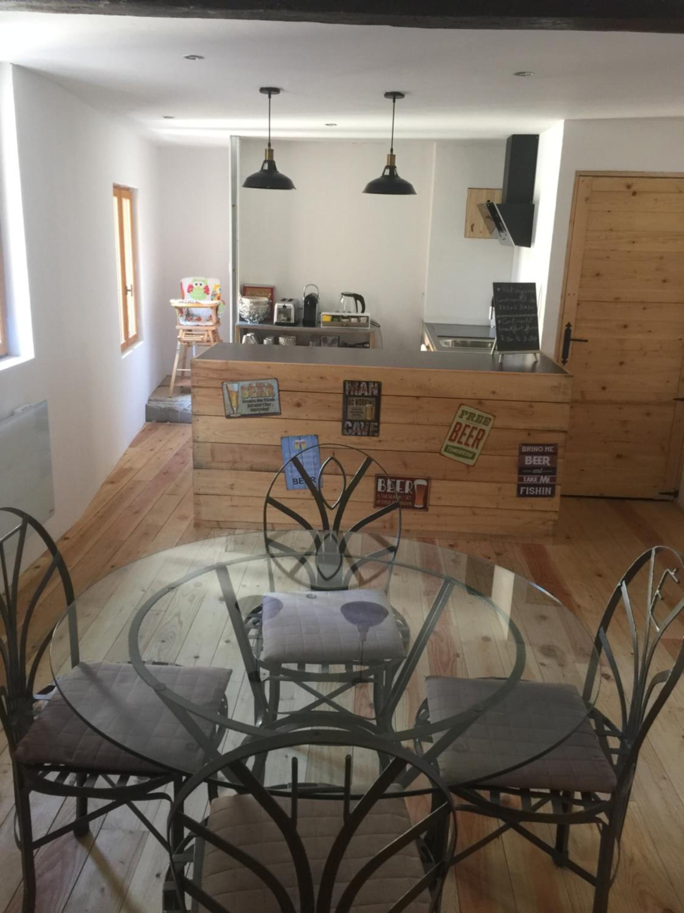 Eine gemütliche Küche mit einer Holzinsel, zwei Pendelleuchten und einem runden Glastisch mit Metallstühlen.