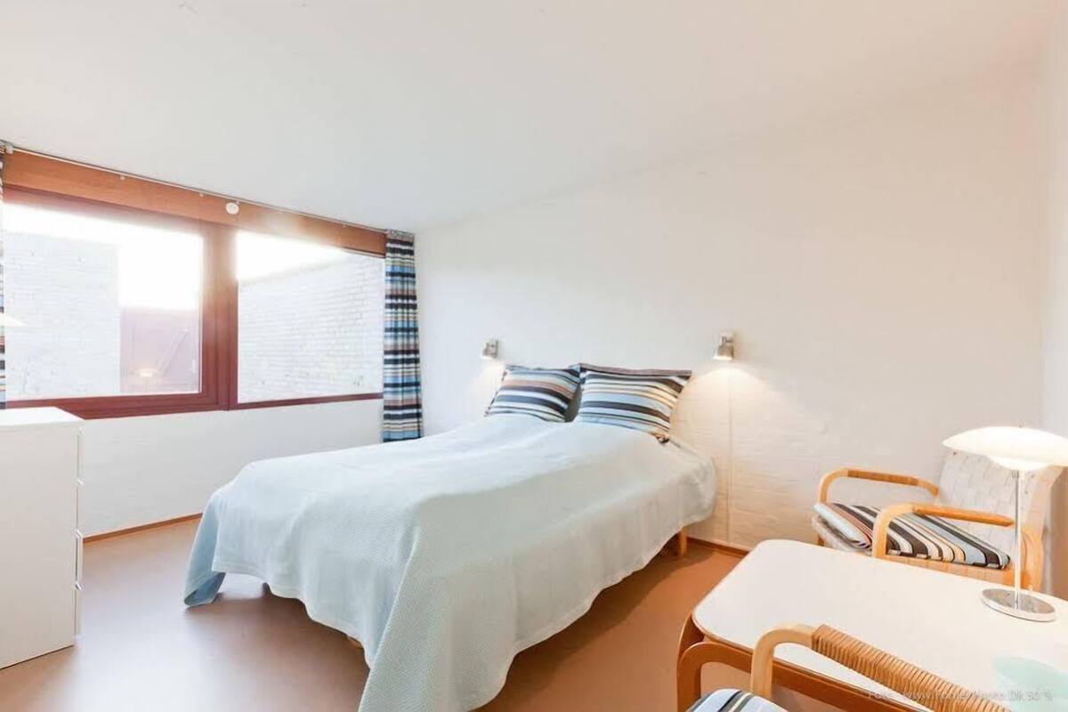A bedroom with a bed, a bedside table, a chair, and a window with curtains.