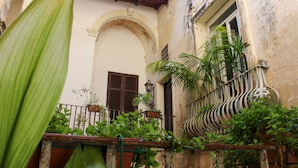 A narrow alley with a building featuring an arched doorway and a balcony with potted plants. - Palazzo Sambiasi (Lecce)