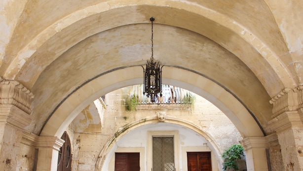 An arched corridor with a hanging chandelier, stone walls, and wooden doors. - Palazzo Sambiasi (Lecce)