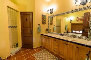 Un baño con puerta de madera, un lavabo con espejo y suelo de baldosas.