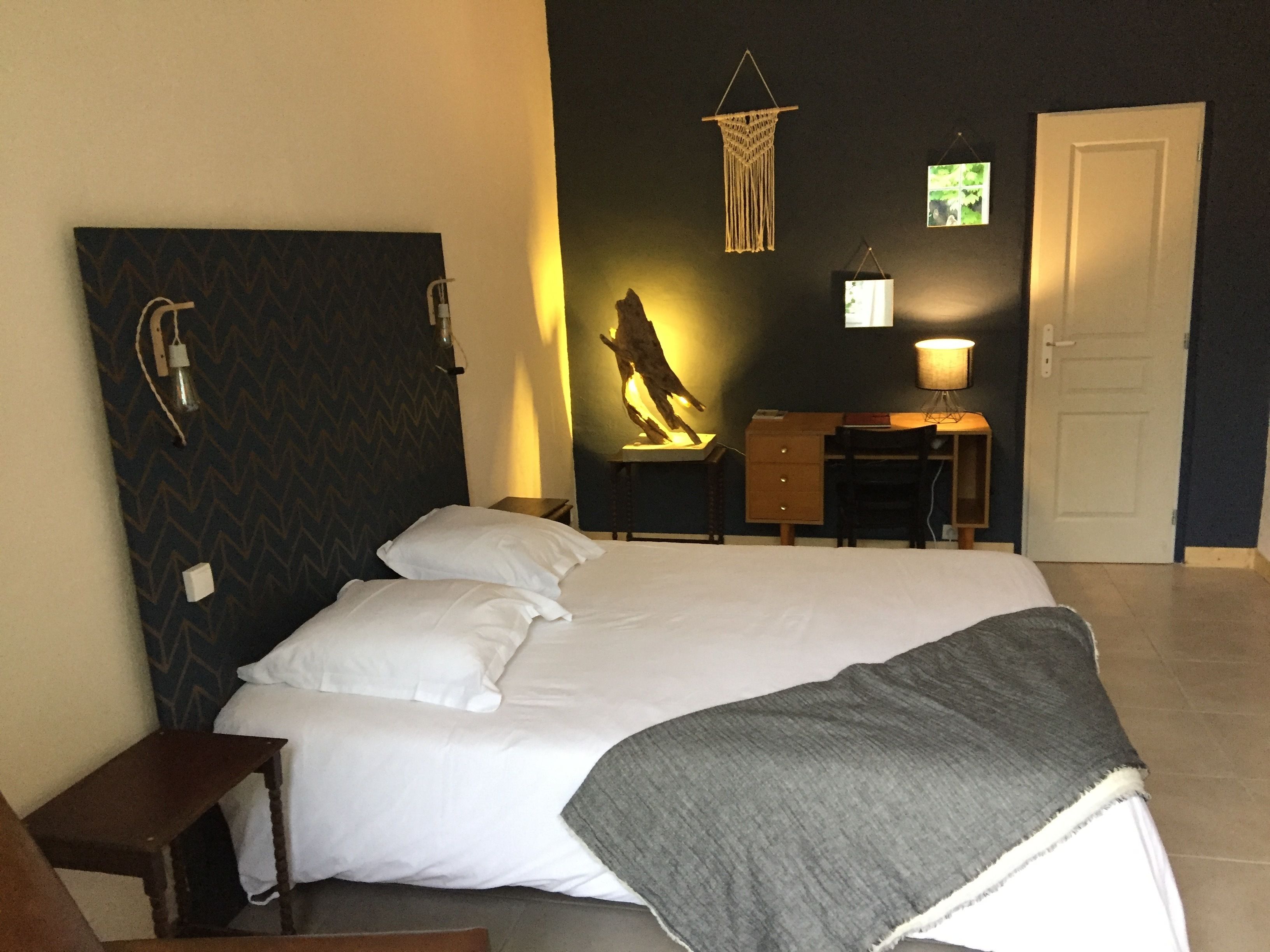 A bedroom with a bed, a desk, a chair, a lamp, and a door.