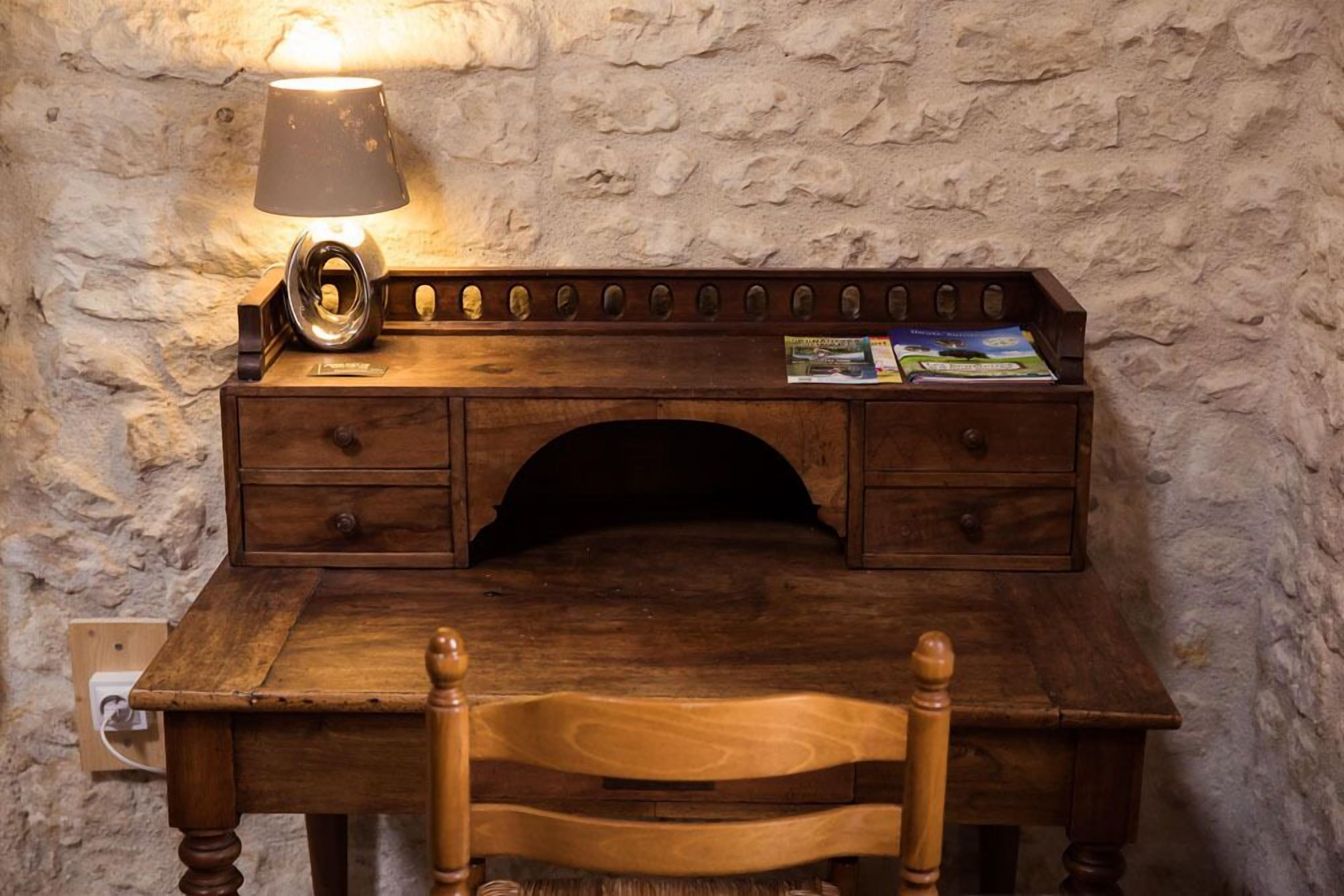 A wooden desk with a lamp, a magazine holder, and a chair.