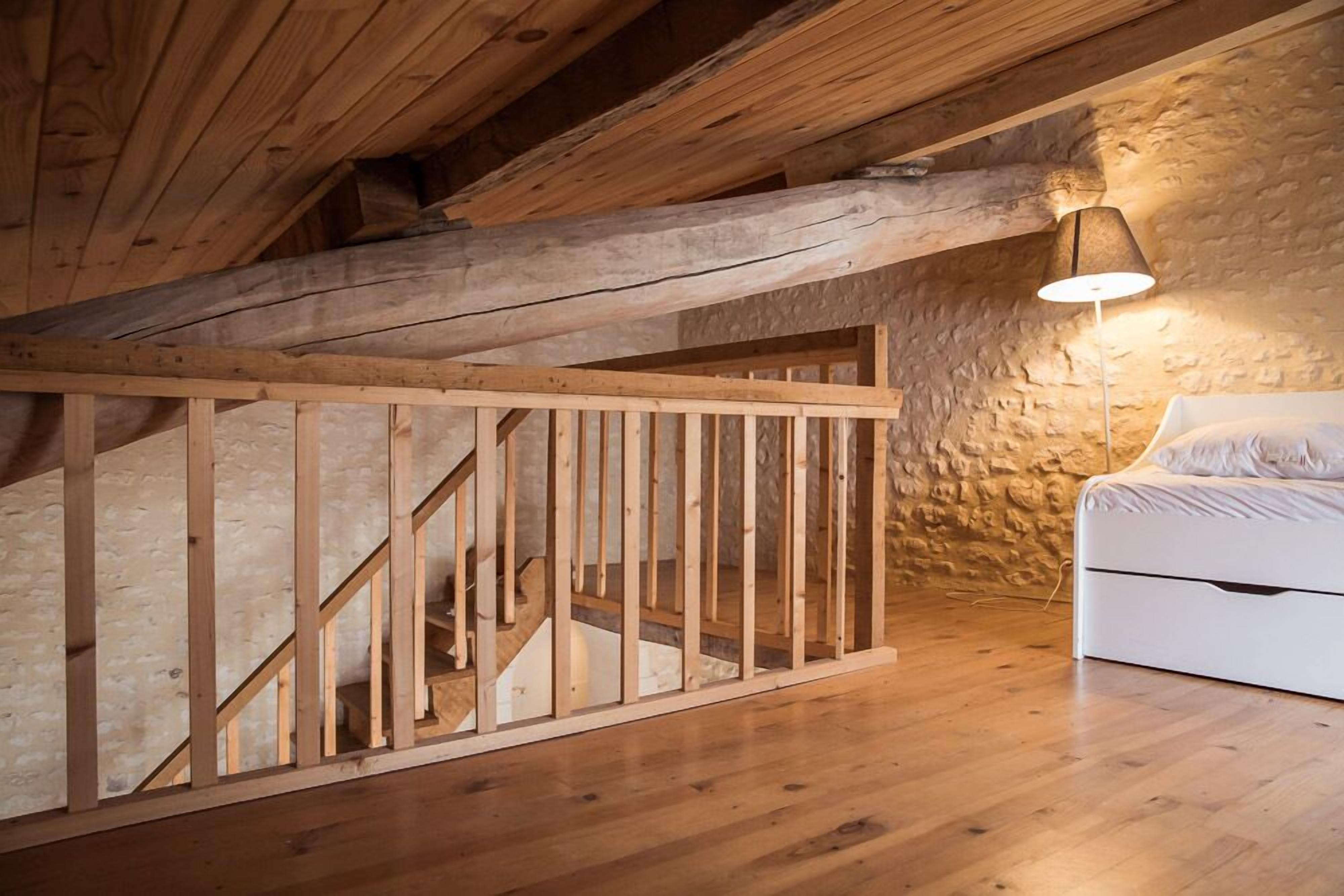 A bedroom with a wooden staircase, a stone wall, and a white bed.