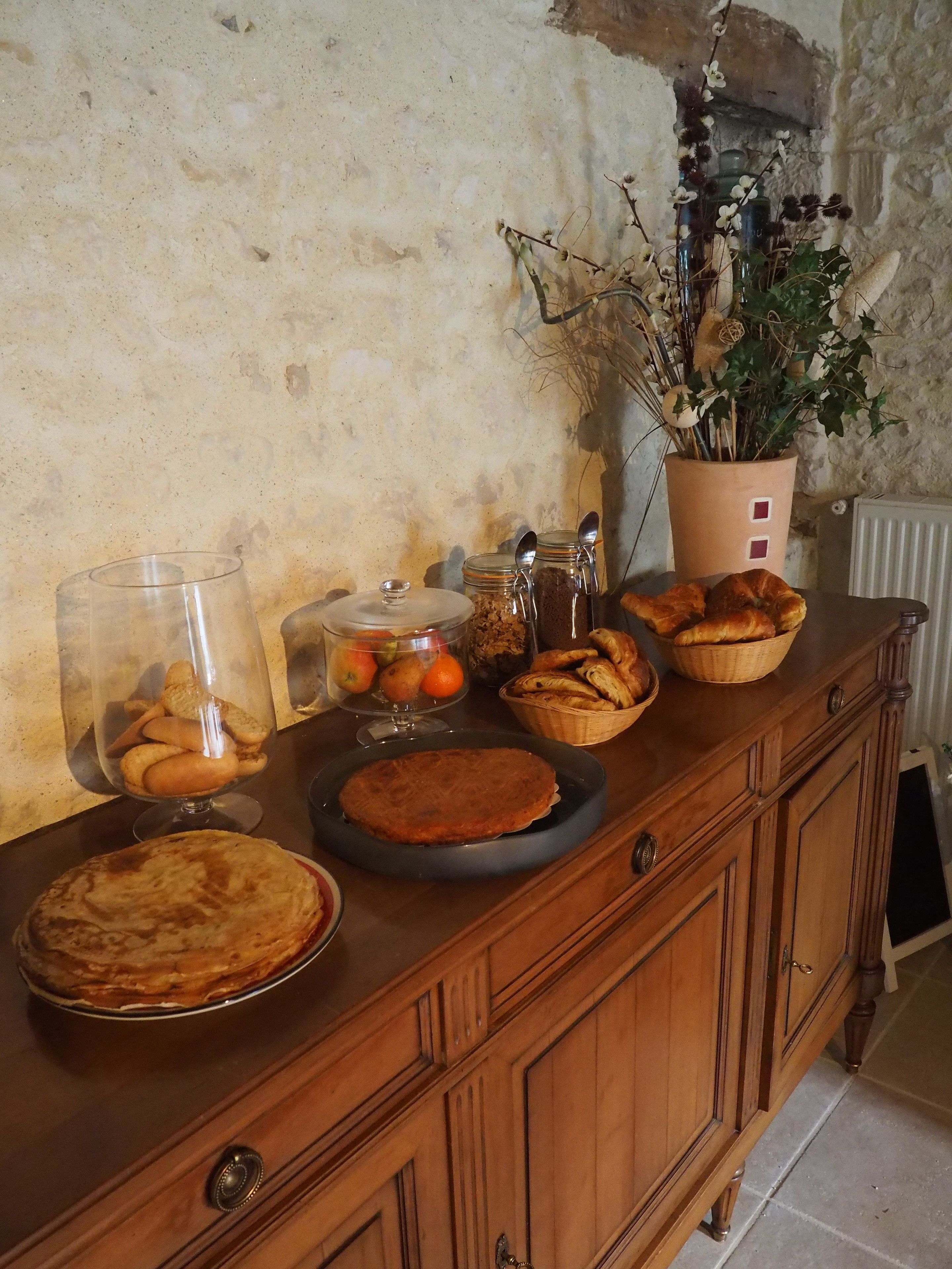 A wooden buffet table with various baked goods, including pies and pastries, and a potted plant with dried branches.