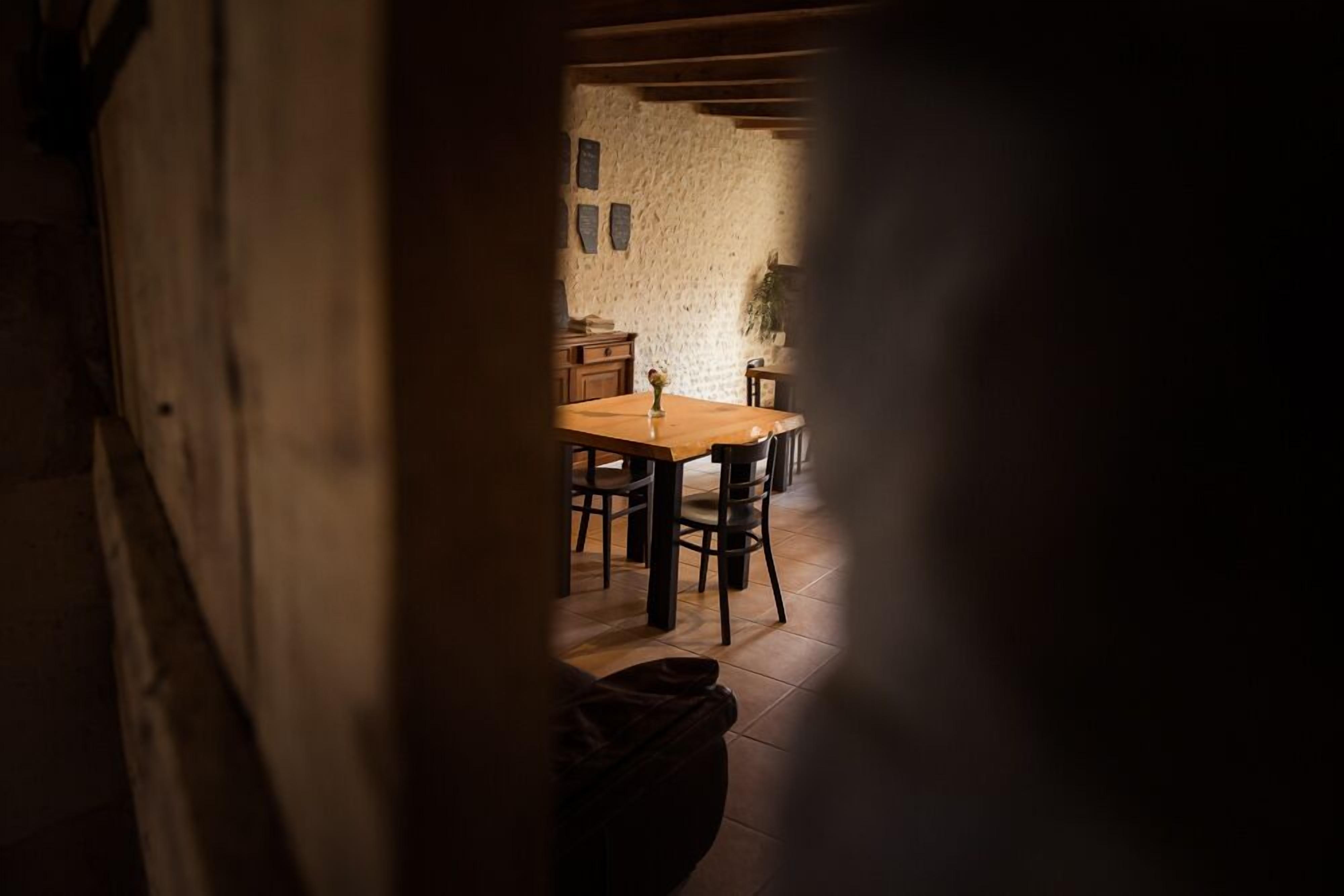 A rustic dining area with a wooden table and chairs, a stone wall, and a hanging plant.