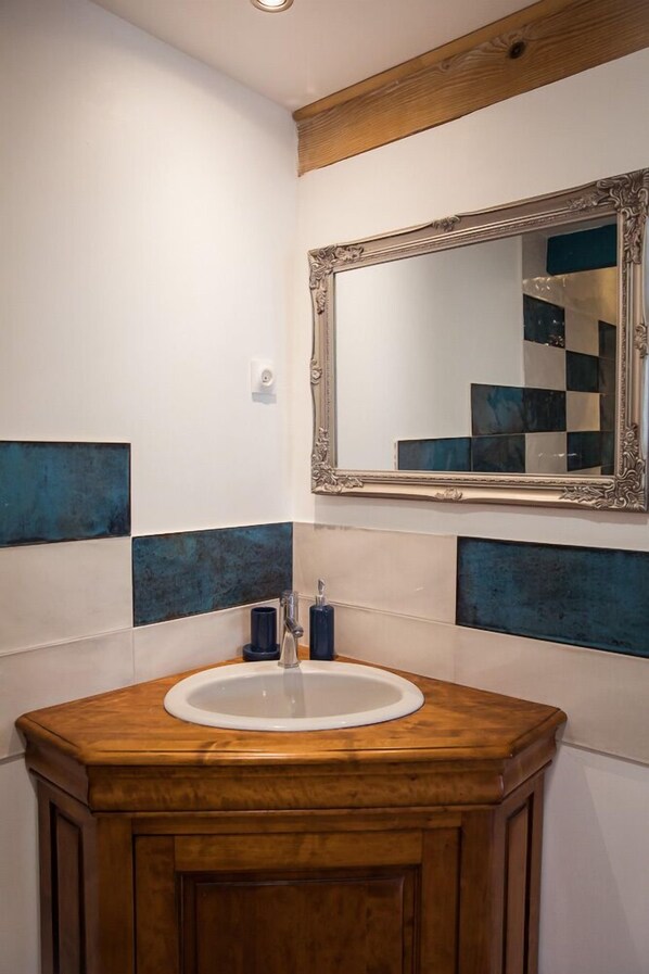Une salle de bain avec un meuble-lavabo en bois, un lavabo blanc et un miroir doté d’un cadre orné.