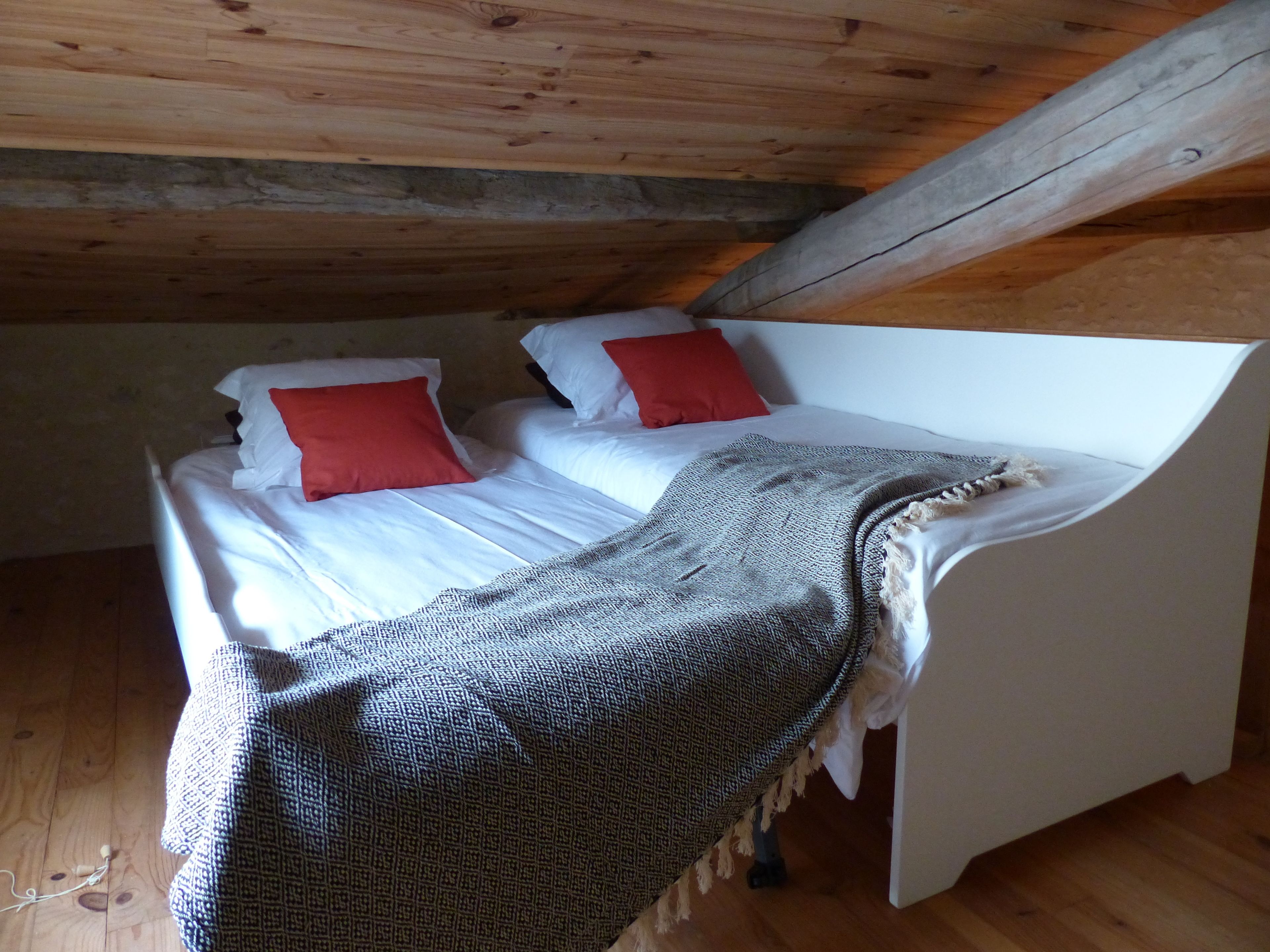 A small, cozy room with a wooden ceiling and a white bed with red pillows.