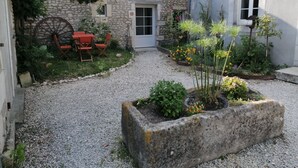 Un edificio de piedra con un patio de grava, un banco de madera y un parterre de flores.