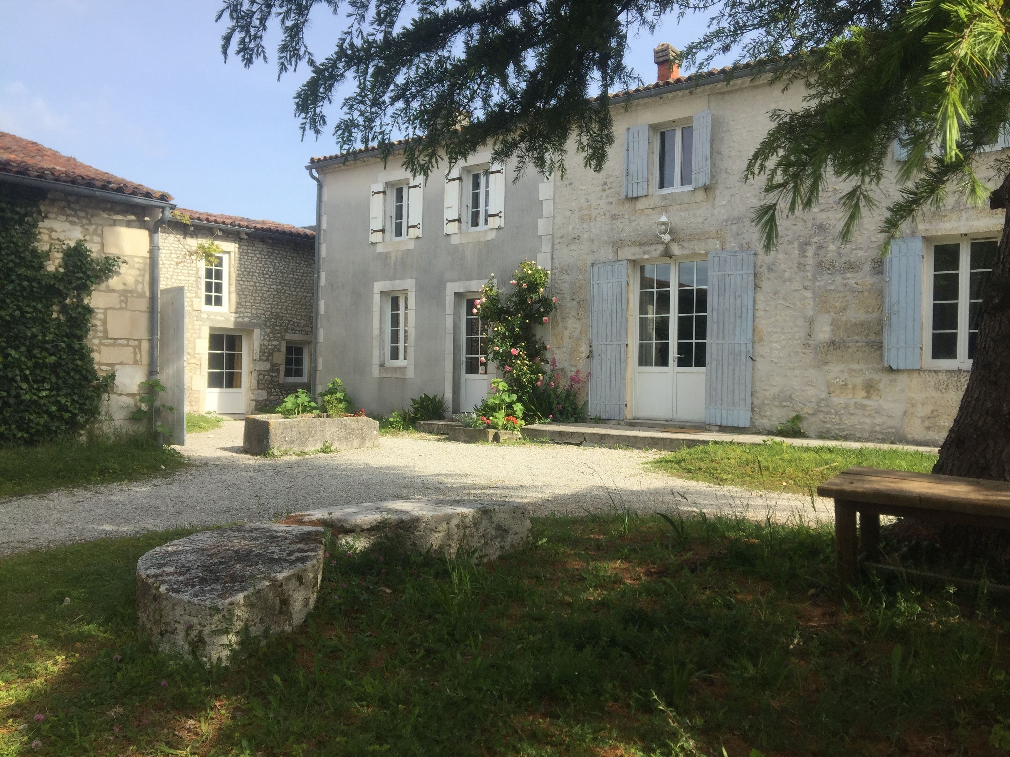 Un bâtiment en pierre avec une cour recouverte de gravier, un banc et un arbre.