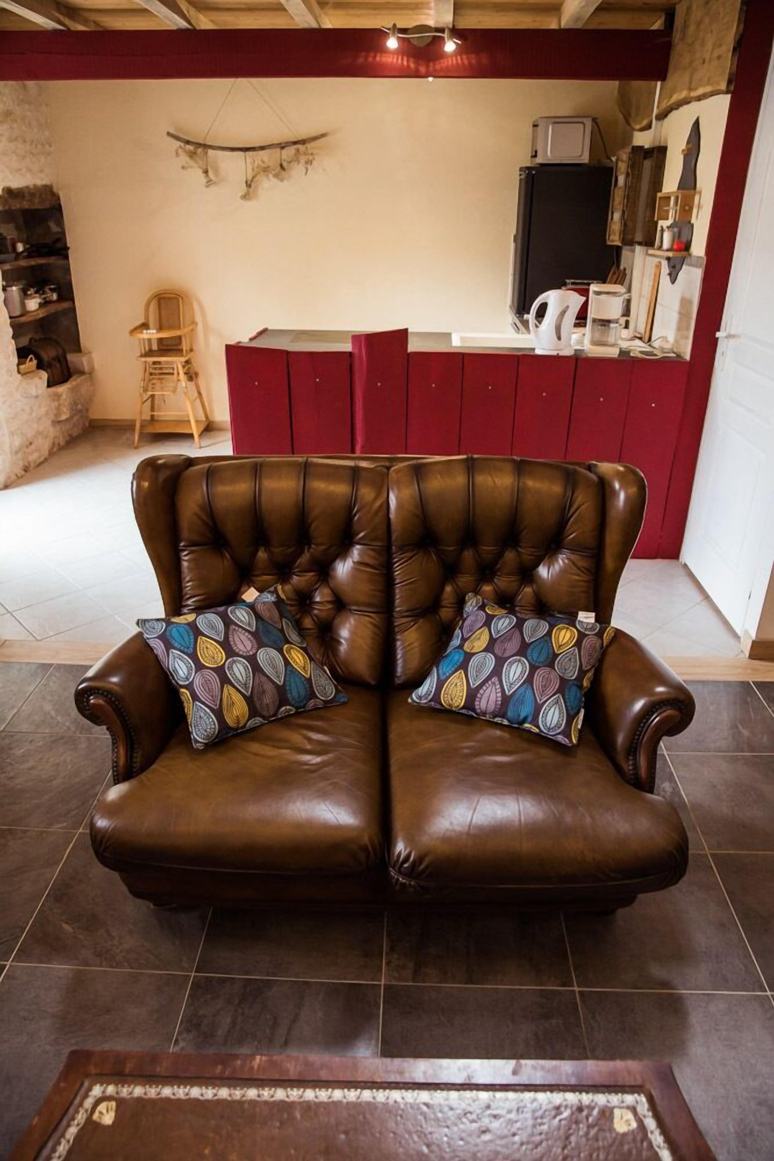 Ein braunes Ledersofa mit zwei gemusterten Kissen in einem Raum, der ein rotes Sideboard und eine Mikrowelle beherbergt.