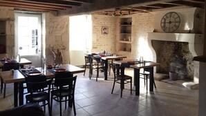 Un comedor rústico con vigas de madera a la vista, paredes de piedra y una chimenea. Las mesas están dispuestas con platos, vasos y cubiertos.