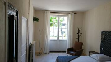 A bedroom with a bed, a chair, a radiator, a window with curtains, and a coat rack.