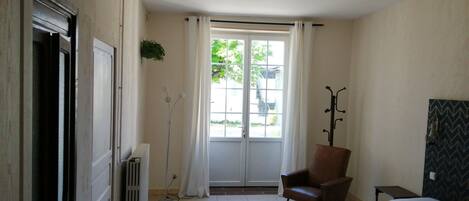 Un dormitorio con cama, una silla, un radiador, una ventana con cortinas y un perchero.