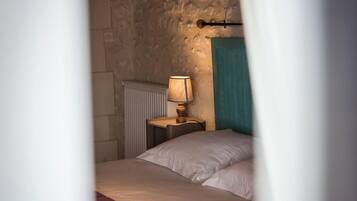 A bedroom with a stone wall, a bed with white bedding, a nightstand with a lamp, and a blue curtain.