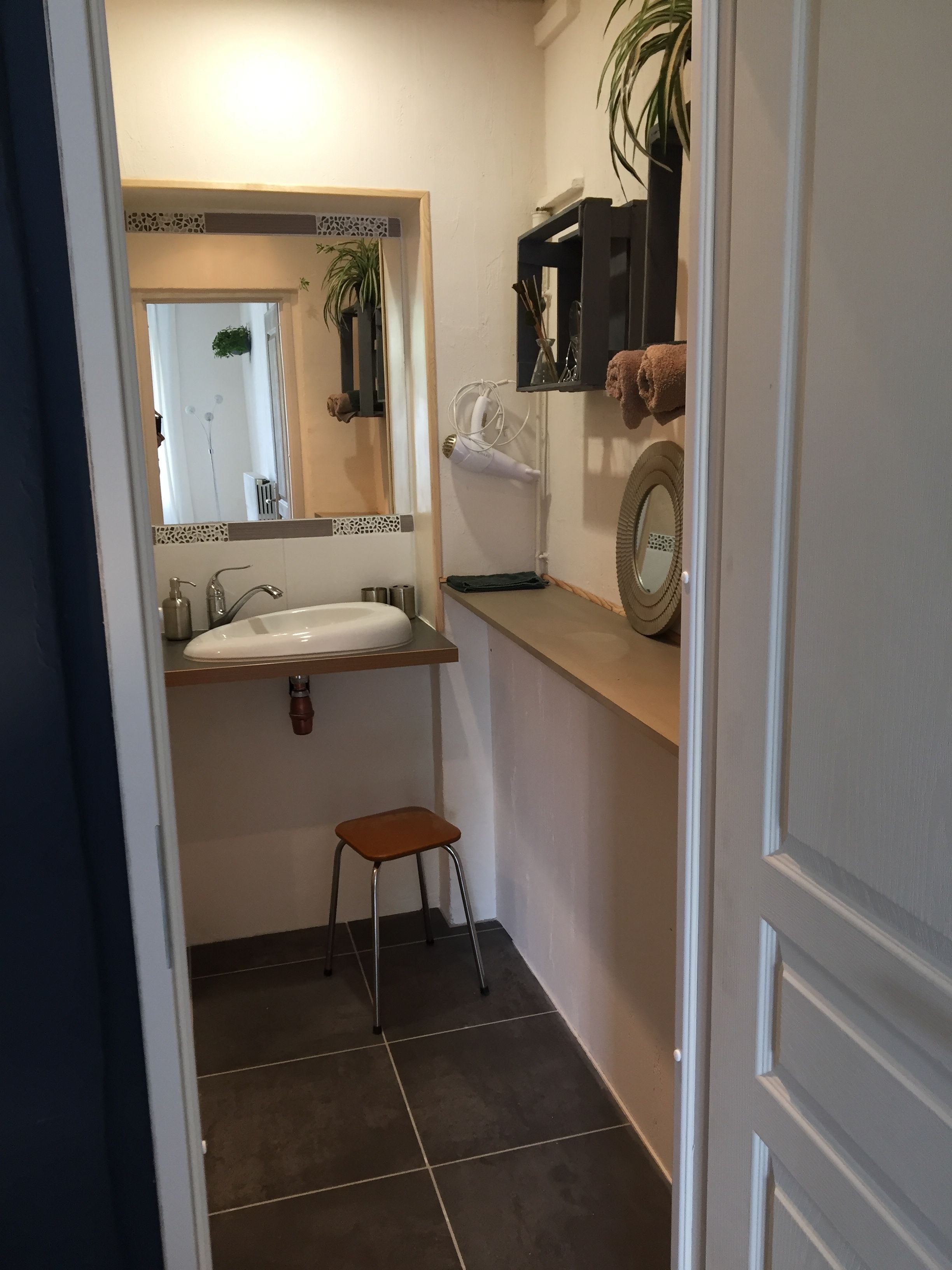 A compact bathroom with a sink, mirror, towel rack, and a small stool.