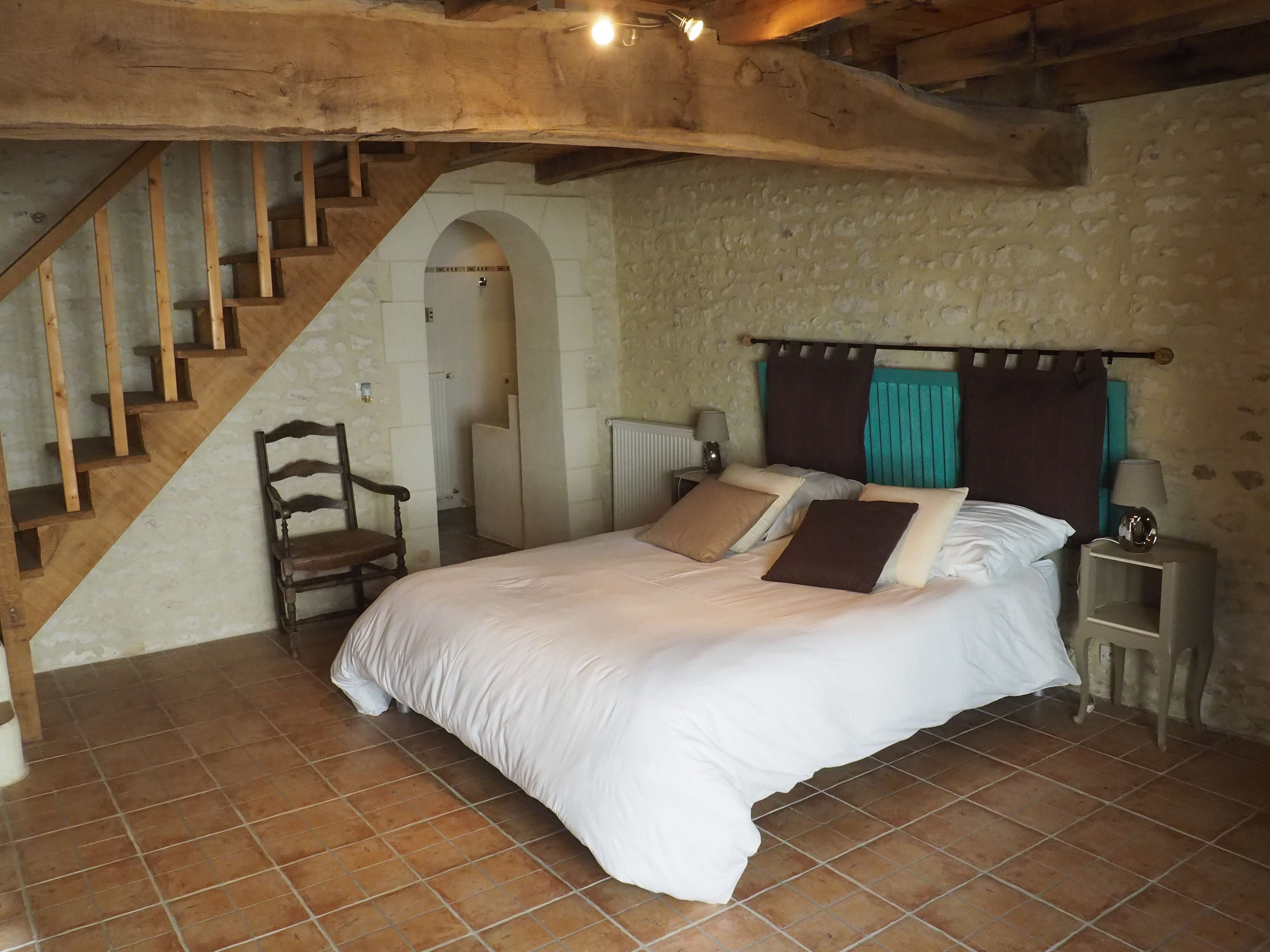 Ein Schlafzimmer mit einer Holztreppe, einem Bett mit vielen Kissen, einem Sessel und einem Nachttisch mit Lampe.