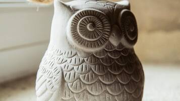 A ceramic owl-shaped container with a rope handle, placed on a textured surface near a window.