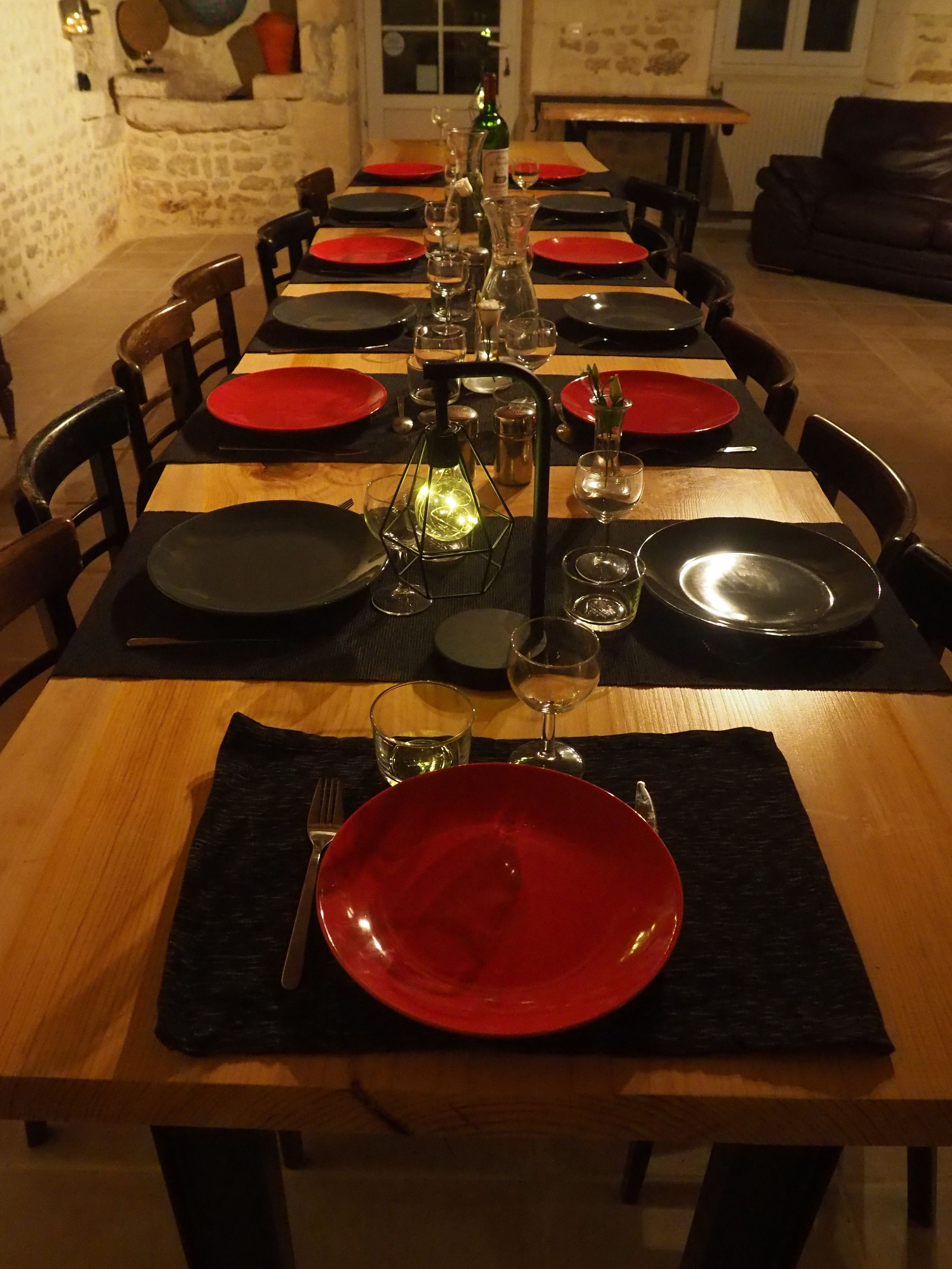 Una mesa de comedor dispuesta con platos rojos y negros, vasos y una botella.