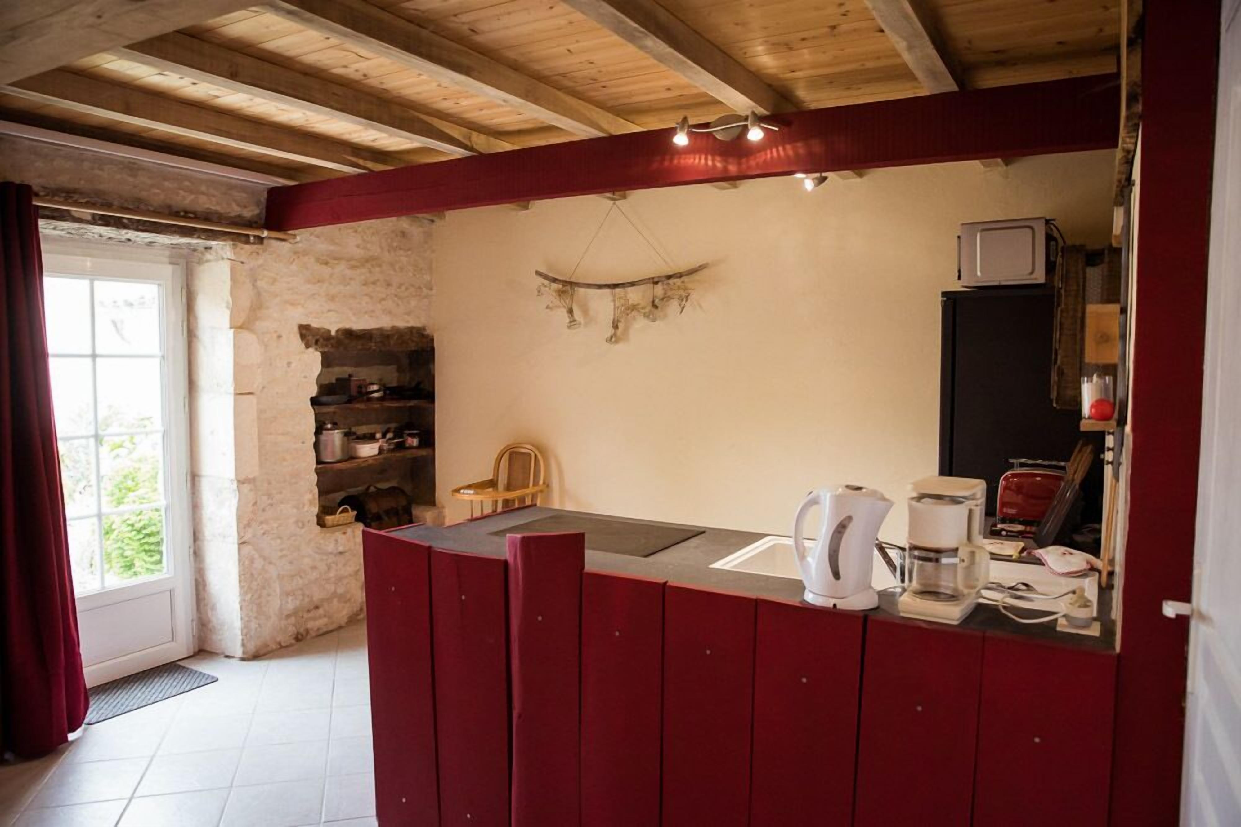A rustic kitchen with a wooden ceiling, a stone wall, and a red counter.