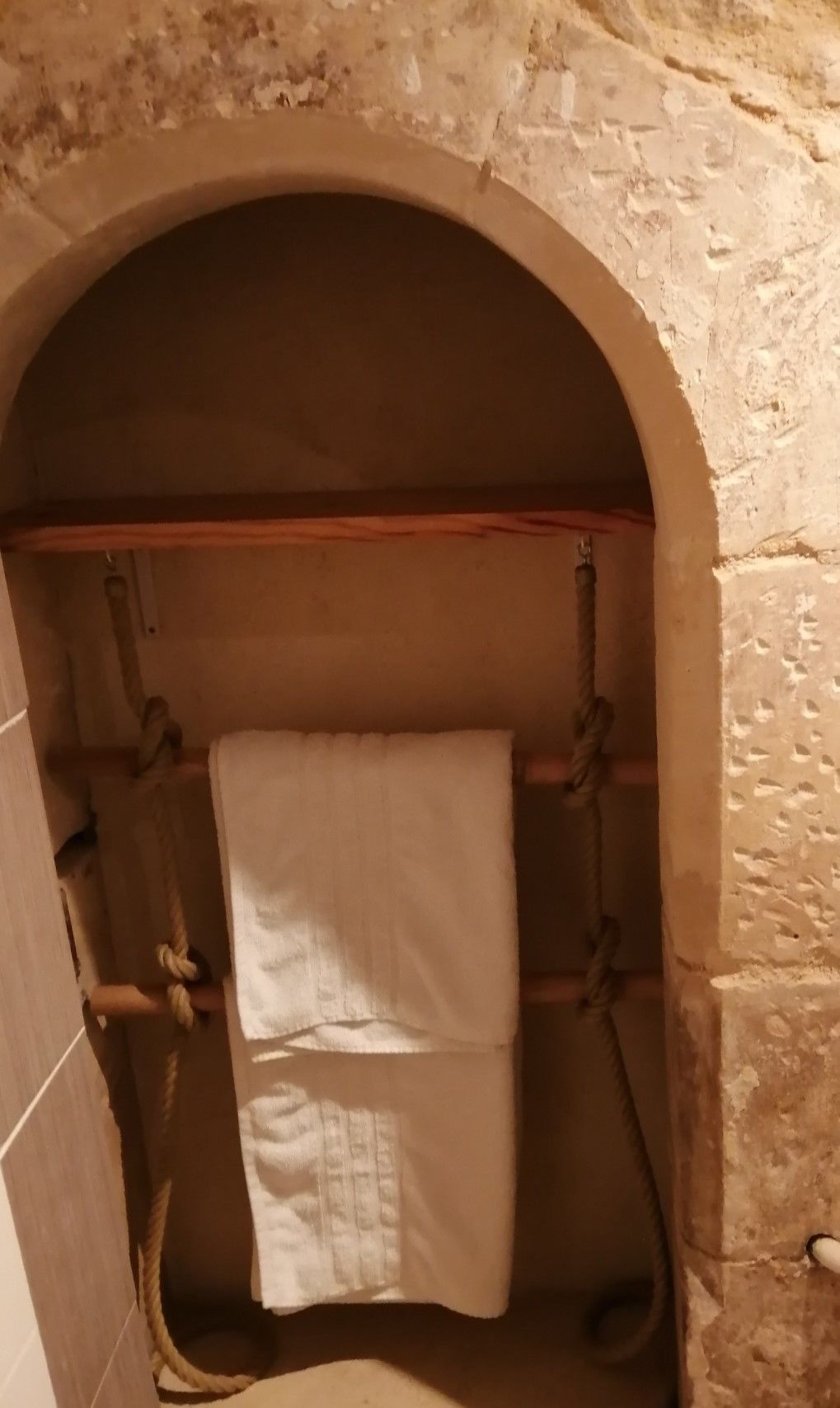 A stone-walled bathroom with a wooden bench, a towel hanging on a hook, and a rope tied to the bench.