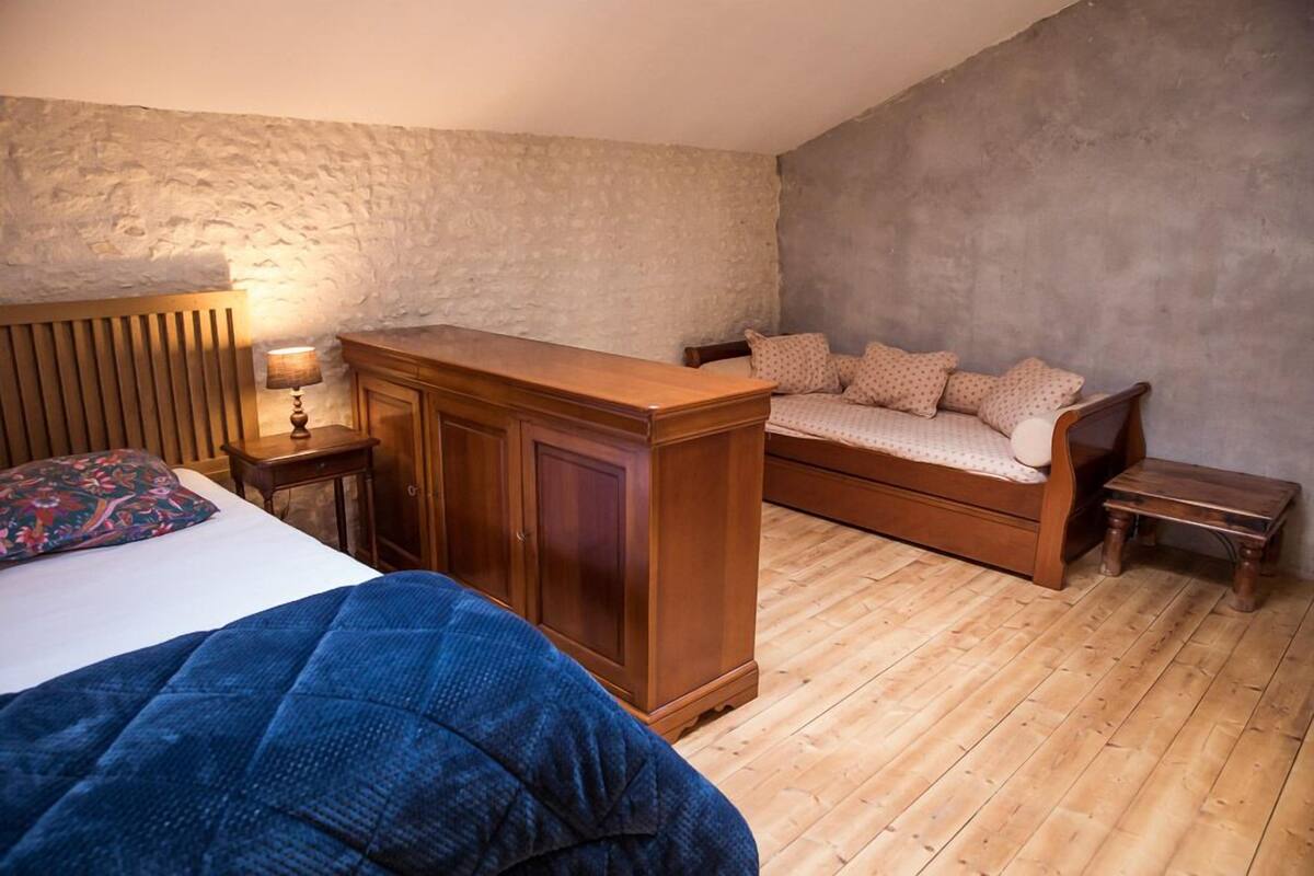 A bedroom with a bed, a wooden dresser, a nightstand, a bench, and a sofa.