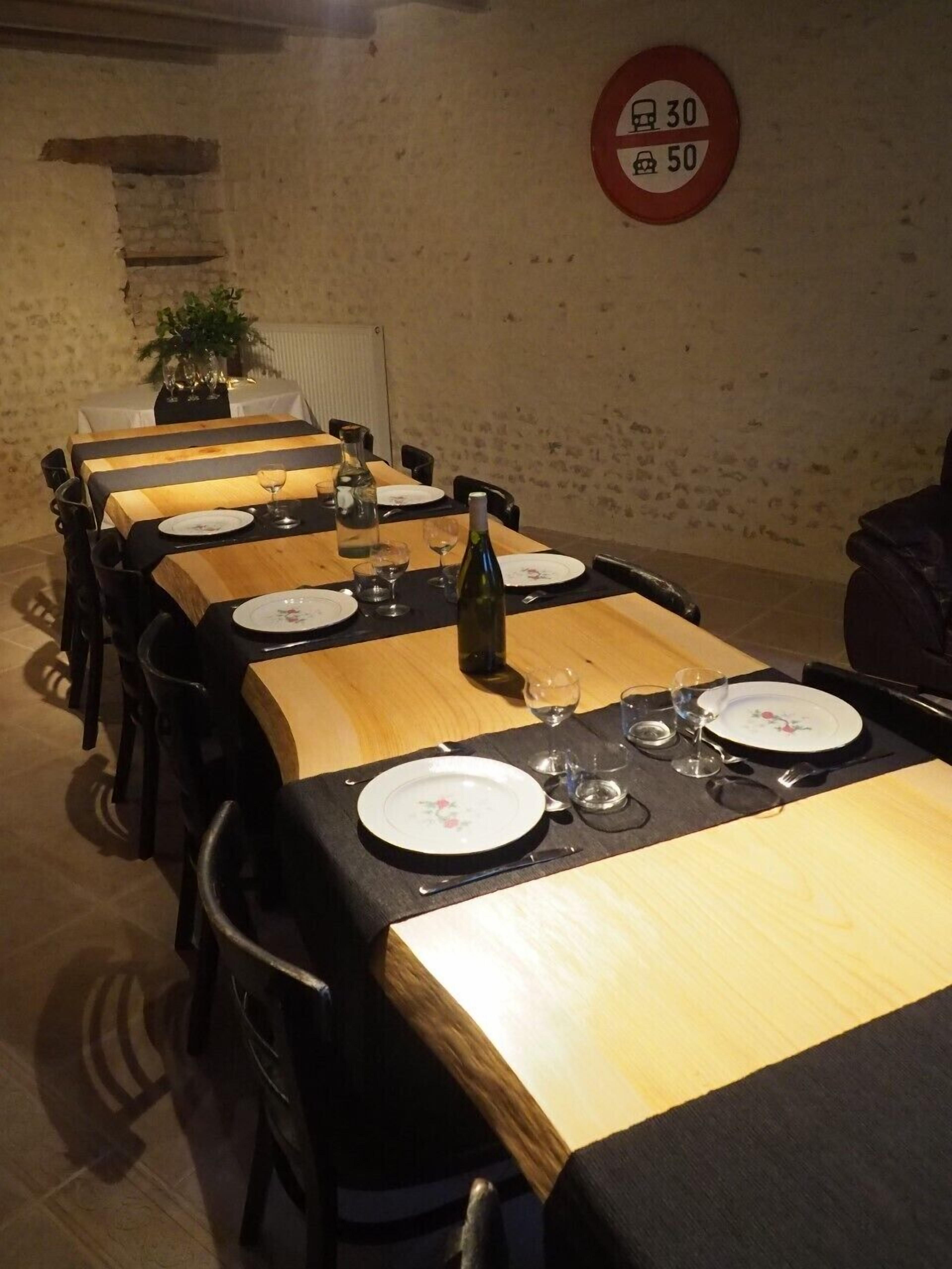 A dining area with multiple tables set for meals, a red circular sign on the wall, and a potted plant in the background.