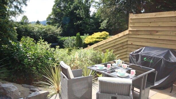 An outdoor patio with wicker furniture, a table set with cups and saucers, and a grill cover.
