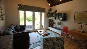 A living room with a sofa, a coffee table, a TV mounted on the wall, and a dining area with a table and chairs.