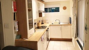 A compact kitchen with white cabinets, a sink, a window, and a clock on the wall.
