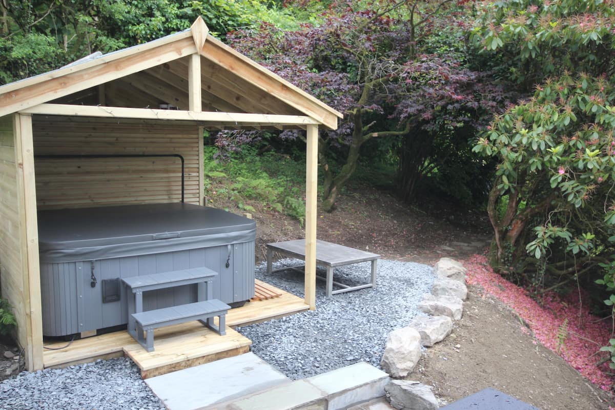 A hot tub in a wooden structure with steps leading up to it, surrounded by gravel and rocks.