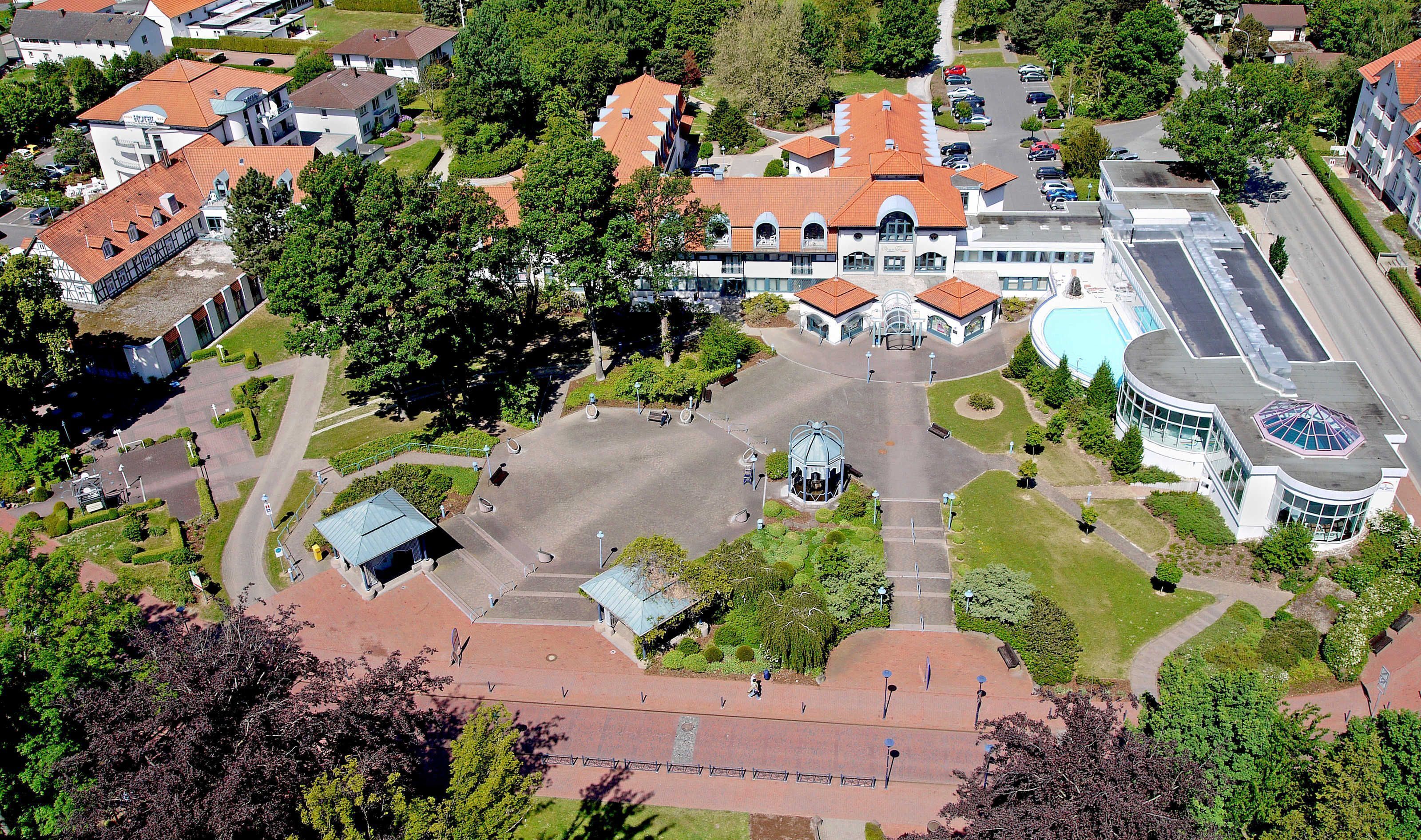 An aerial view of a residential area with a central courtyard, surrounded by houses with red-tiled roofs, and a large building with a dome structure.