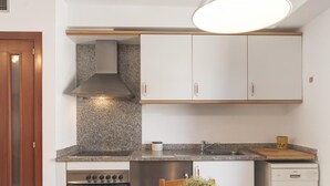 Une cuisine compacte avec des meubles blancs, un plan de travail en granit, un four encastré et un lave-vaisselle.