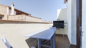 Une terrasse extérieure avec une table et des chaises, un barbecue et une vue sur les bâtiments en arrière-plan.