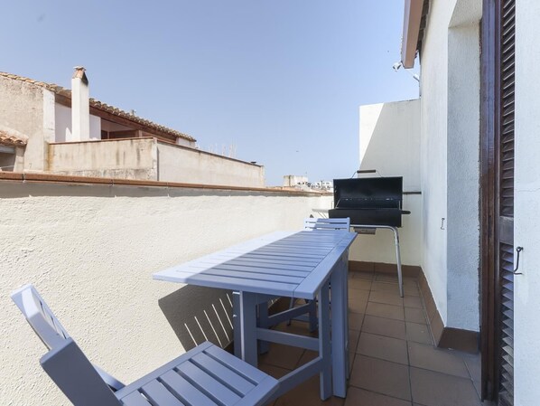 An outdoor patio with a table and chairs, a barbecue grill, and a view of buildings in the background.