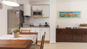 Une cuisine compacte avec des meubles blancs, un four à micro-ondes et une machine à café posés sur le plan de travail.