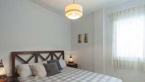 Une chambre à coucher avec un lit, une table de chevet, une lampe et une fenêtre avec des rideaux.