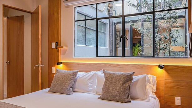 Un dormitorio con un ventanal grande, cabecera de madera y una mesita de noche.