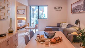 Una habitación moderna con una mesa de comedor dispuesta con comida y bebidas, un sofá, una cama y un ventanal grande.