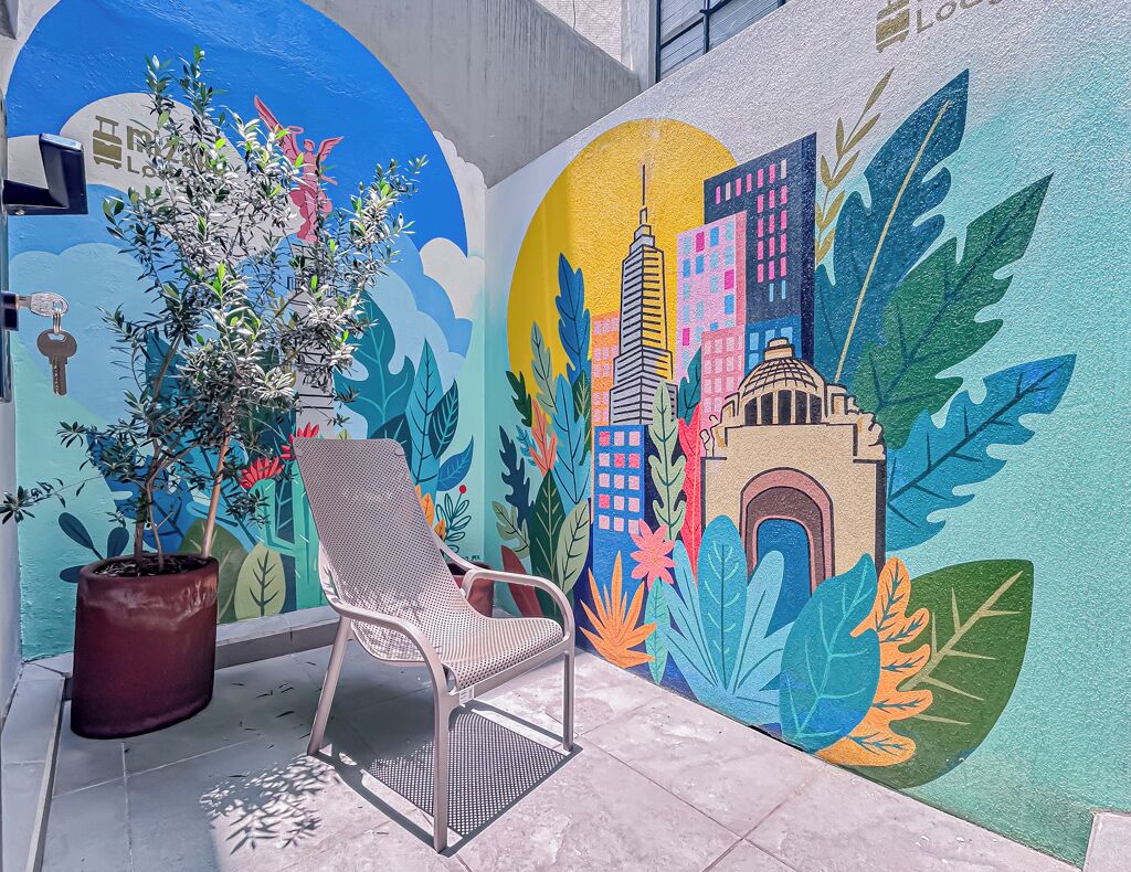 A mural with a cityscape, a potted plant, and a metal chair.